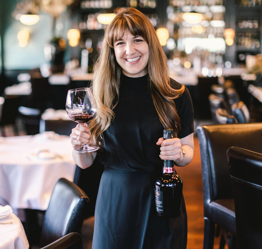 Woman smiling, holding a glass of red wine and a bottle of rosé Champagne